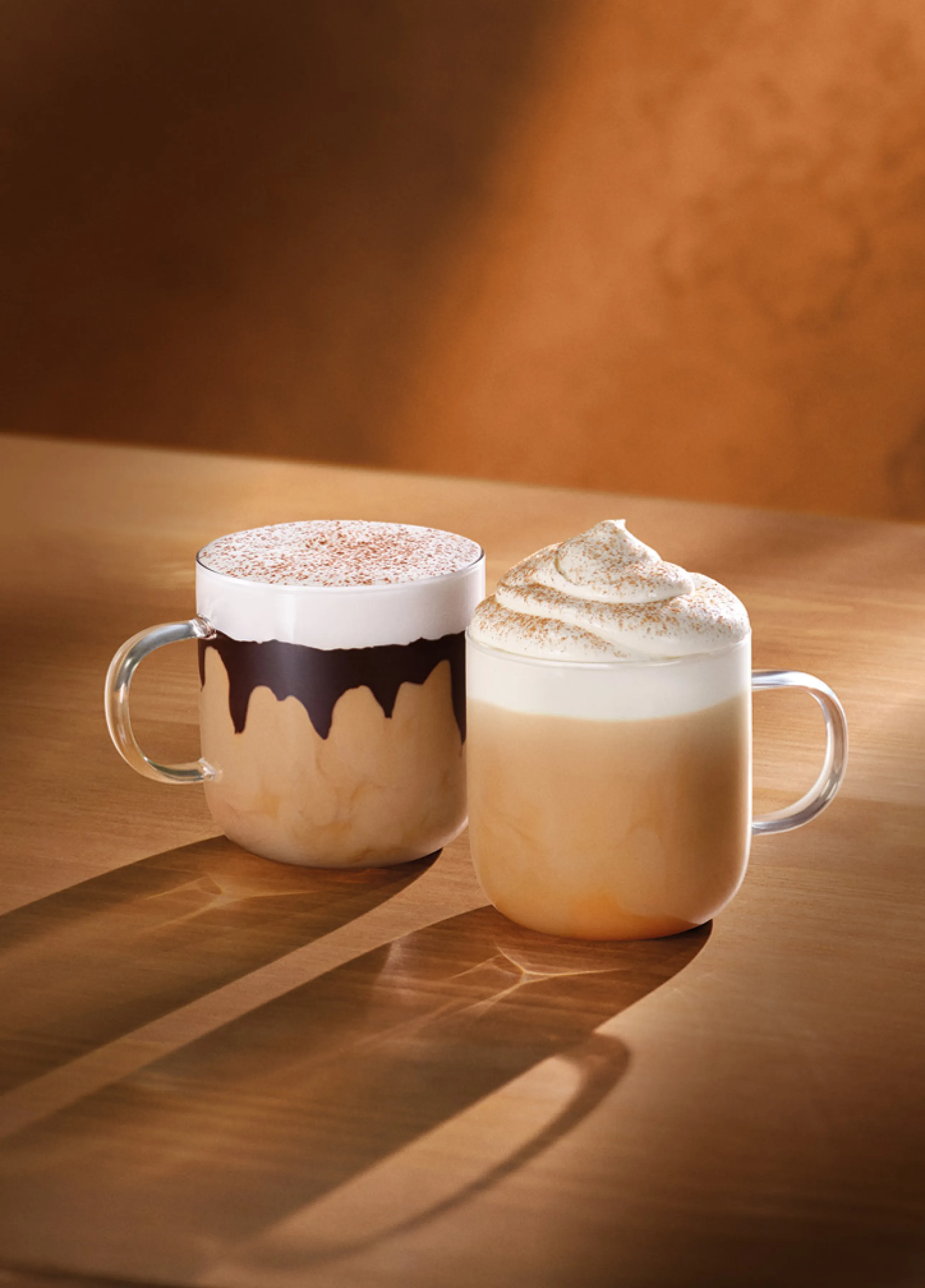 Duas bebidas da Starbucks em cima de uma mesa com tons de outono: o Tiramisu Velvet Latte e o Pumpkin Spice Latte.