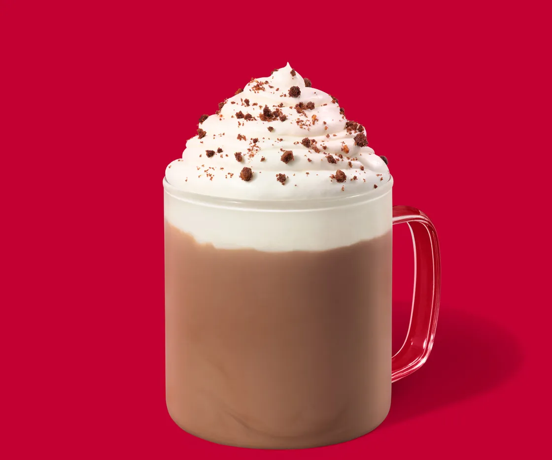 Fudge Brownie Hot Chocolate quente com nata numa chávena de vidro, sobre um fundo vermelho