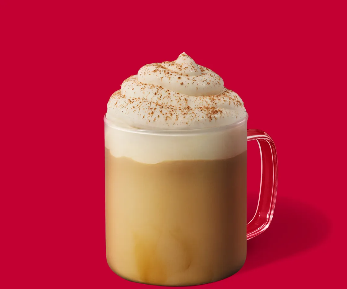 Gingerbread Latte quente com nata numa chávena de vidro, sobre um fundo vermelho