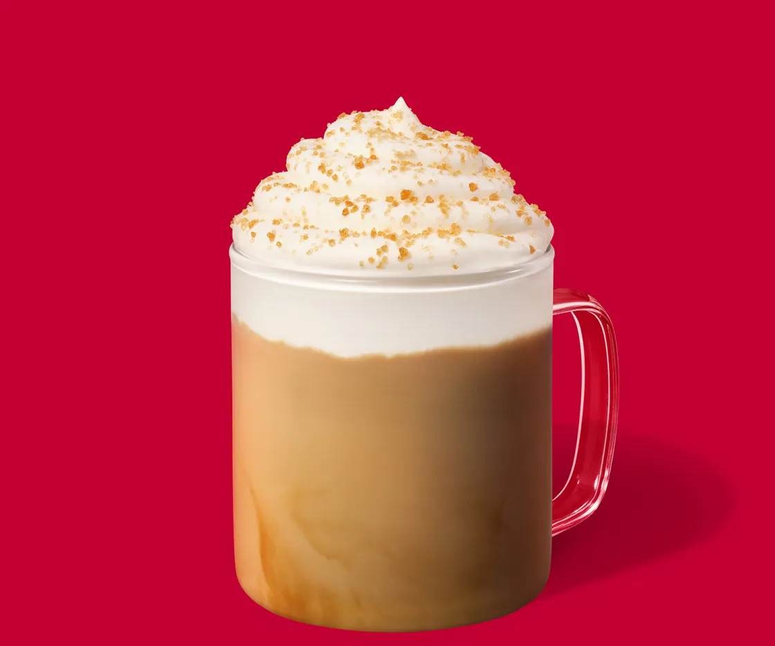 Toffee Nut Latte quente com nata numa chávena de vidro sobre um fundo vermelho