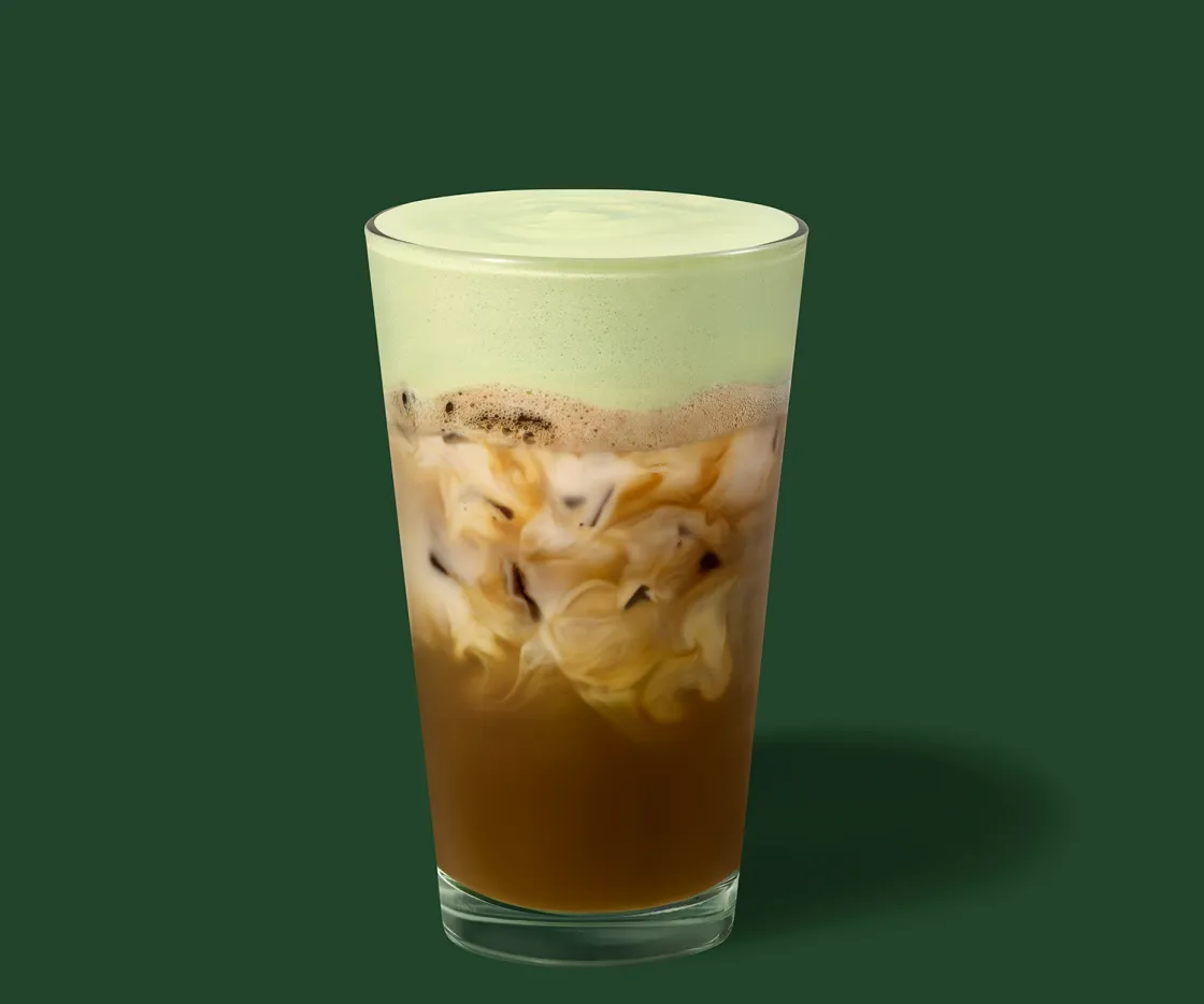 Um espresso batido gelado de pistácio e aveia num copo de vidro, com fundo verde.
