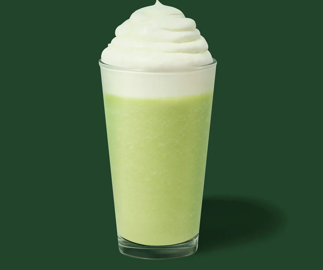 Um Frappuccino de pistácio com natas num copo de vidro, com fundo verde.