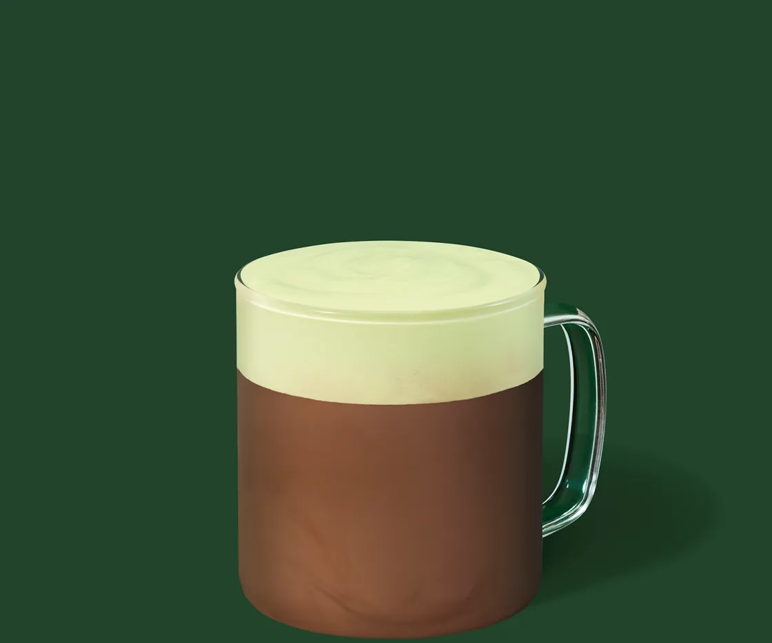 Um chocolate quente de pistácio numa chávena de vidro, com fundo verde.