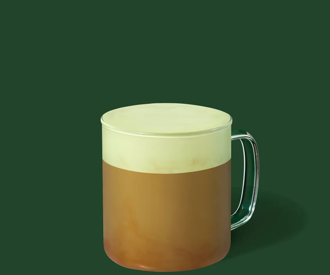 Um pistácio velvet latte quente numa chávena de vidro, com fundo verde.
