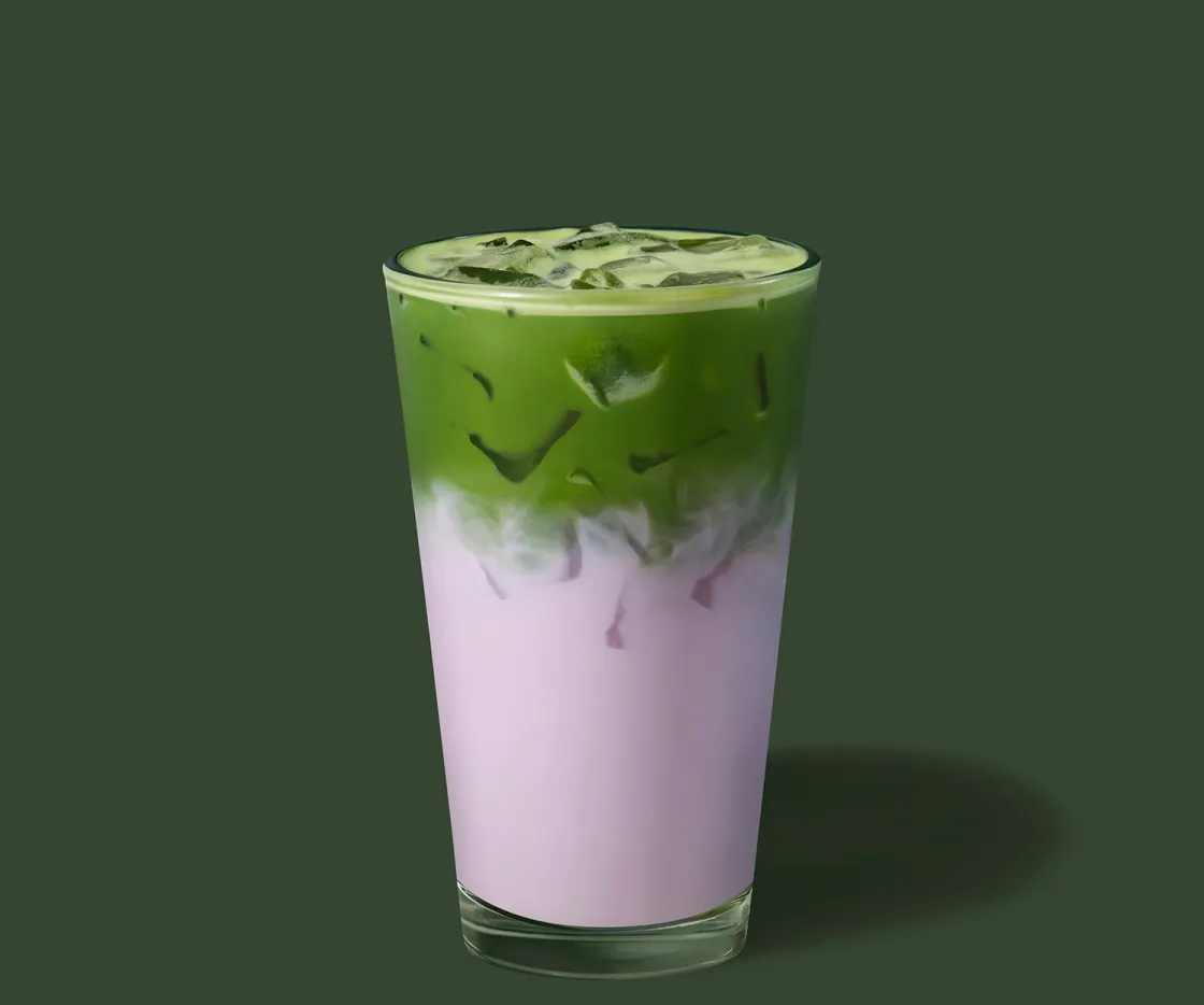 Um copo de vidro com gelo com Ube Vanilla Velvet Matcha Latte sobre fundo verde